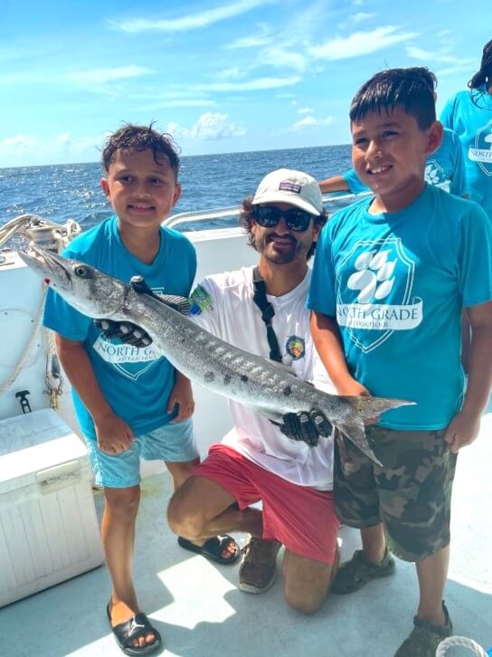 Fishing boat crew helping students show off their catch.